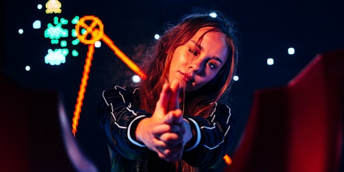 A woman with her fingers in the shape of a gun infront of gaming-style neon signs A woman with her fingers in the shape of a gun infront of gaming-style neon signs