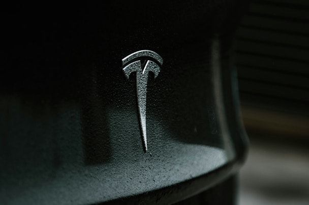 A rain-flecked Tesla badge on a grey car A rain-flecked Tesla badge on a grey car