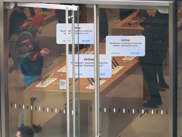 AirDrop messages promoting BackMarket, superimposed on top of an image of customers in an Apple Store AirDrop messages promoting BackMarket, superimposed on top of an image of customers in an Apple Store