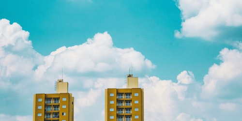 The tops of two yellow tower blocks stand before clouds in a blue sky The tops of two yellow tower blocks stand before clouds in a blue sky