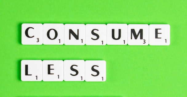 Scrabble letter pieces spell out the message 'consume less' against a green background Scrabble letter pieces spell out the message 'consume less' against a green background