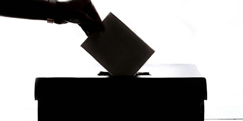 A hand places a voting paper into a ballot box A hand places a voting paper into a ballot box