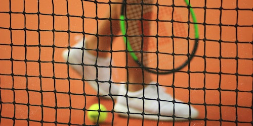 A tennis player and ball behind a tennis net A tennis player and ball behind a tennis net