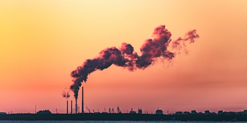 A factory against an orange sky, producing a plume of smoke A factory against an orange sky, producing a plume of smoke