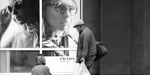 A man in a sleeping bag in front of a Prada store A man in a sleeping bag in front of a Prada store