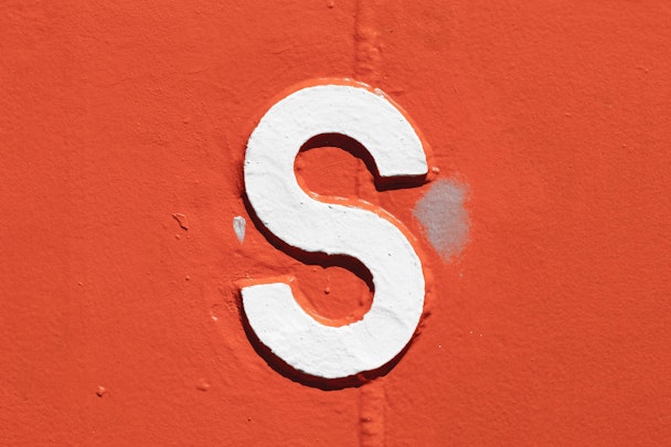 A white letter 's' with a black outline painted onto an orange wall A white letter 's' with a black outline painted onto an orange wall