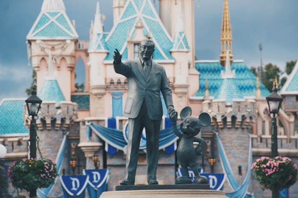 A statue of Walt Disney and Mickey Mouse, in front of a Disney pleasure resort A statue of Walt Disney and Mickey Mouse, in front of a Disney pleasure resort