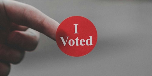 A sticker reading 'I voted' on the end of someone's finger A sticker reading 'I voted' on the end of someone's finger